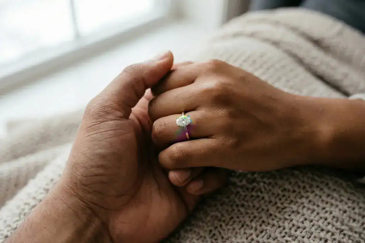 Couple holding hands with oval diamond engagement ring showing rainbow light dispersion