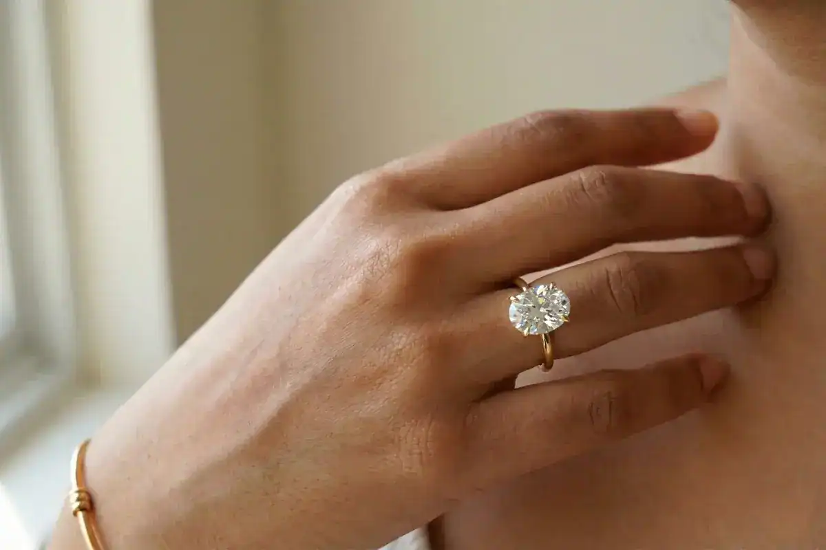 Oval diamond solitaire engagement ring in 18K yellow gold on woman's hand